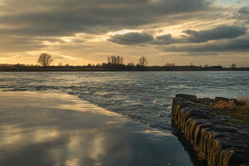 Spiegelend water gaat over in een naad van woelig stromend water, met een stenen krib